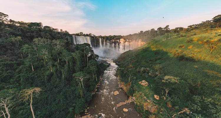Vue aérienne d'une puissante cascade de forêt tropicale plongeant dans une gorge fluviale entourée d'une jungle dense et verdoyante à l'heure dorée.