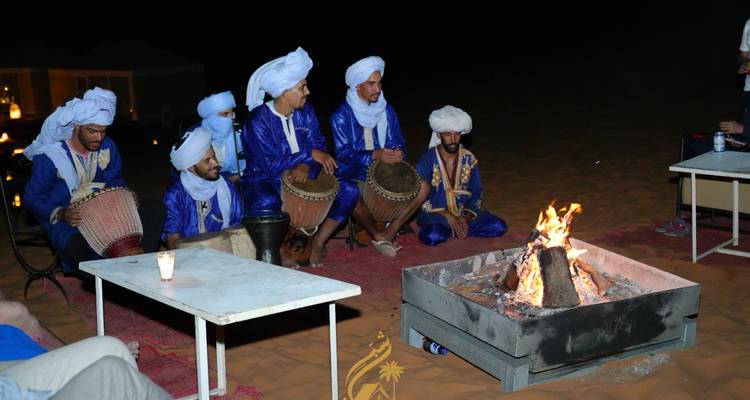 Groupe d'hommes en tenue traditionnelle jouant du tambour autour d'un feu la nuit.