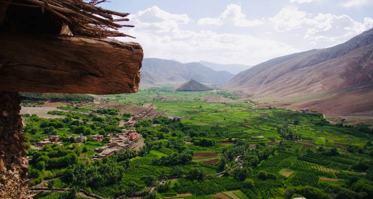 Vue large d'une vallée luxuriante avec des champs et des montagnes.