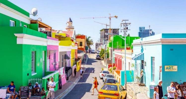 Bunt bemalte Kolonialhäuser säumen die schmale Straße von Kapstadts Bo-Kaap, während Einheimische draußen entspannen.