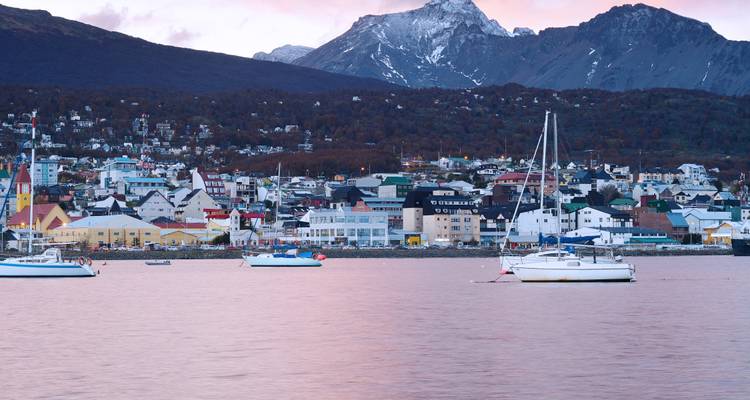 Bateaux dans une baie avec une ville et des montagnes en arrière-plan au coucher du soleil.