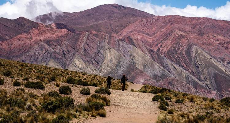 Deux randonneurs marchant vers des formations montagneuses colorées.