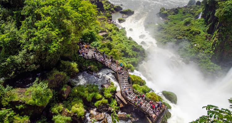 Touristen auf einem Gehweg mit Blick auf einen mächtigen Wasserfall.