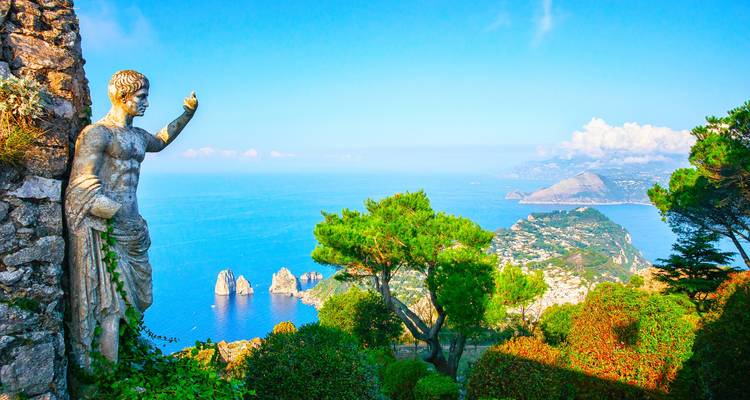 Statue mit Blick auf die azurblauen Gewässer und die hoch aufragenden Felsnadeln von Capri aus einem üppigen Klippengarten.