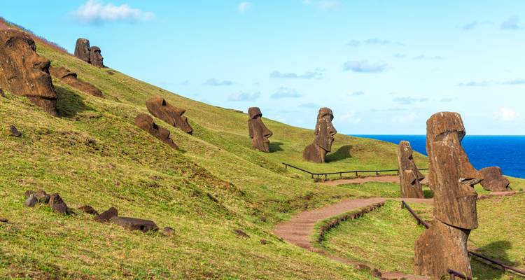 Numerosas estatuas Moai a lo largo de laderas cubiertas de hierba con vista al océano.