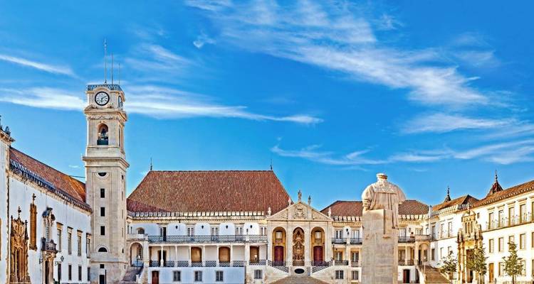 Heller Innenhof der Universität Coimbra mit Glockenturm und Statue unter einem leuchtend blauen Himmel.