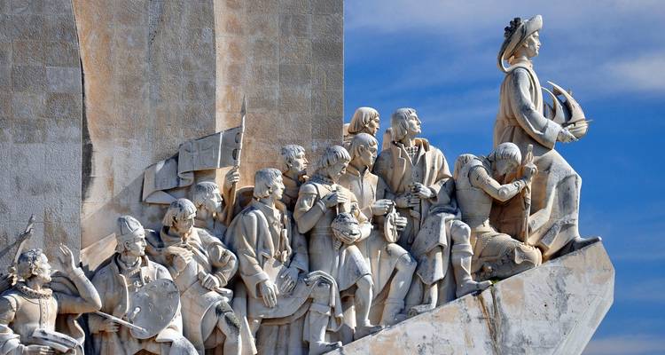 Steinstatuen portugiesischer Entdecker am Denkmal der Entdeckungen vor blauem Himmel.