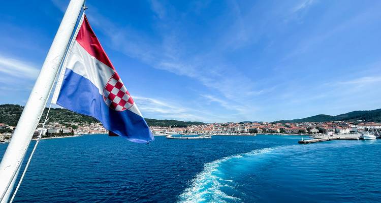 Un drapeau croate sur un ferry avec une ville côtière en arrière-plan