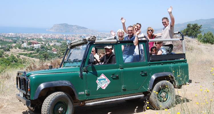 Grupo de personas en un jeep de safari saludando con vista de un pueblo al fondo.