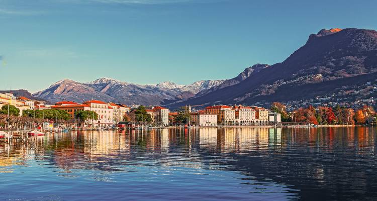 Ville lacustre aux façades colorées se reflétant dans l'eau calme sous des collines escarpées au coucher du soleil.