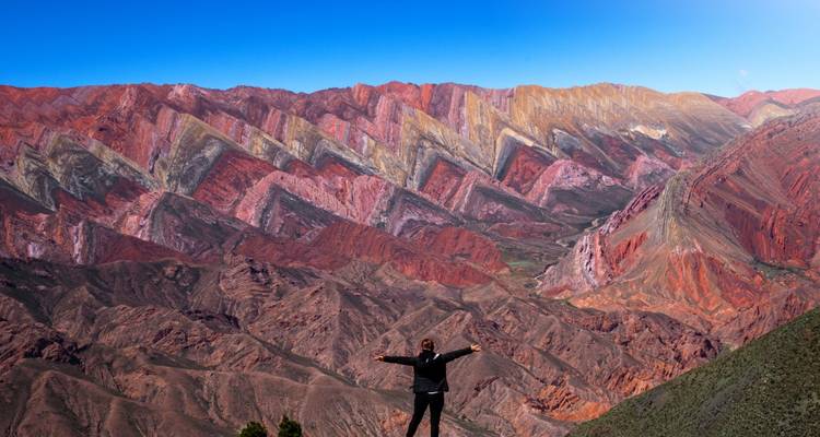 Persoon met open armen staand voor een kleurrijk berglandschap.