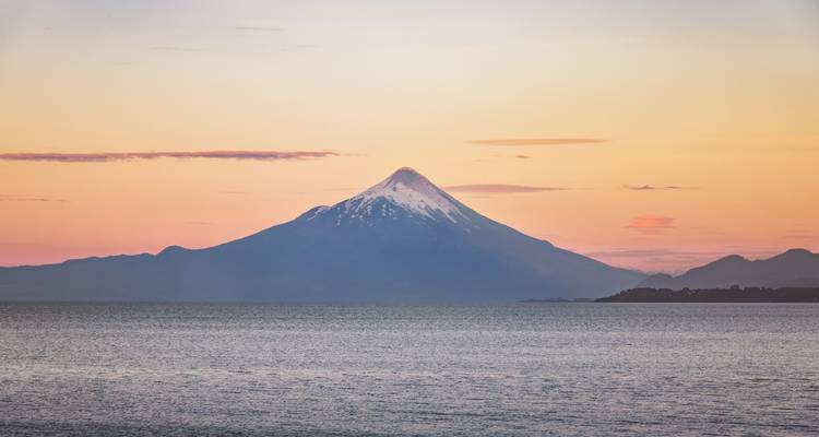 Volcan au coucher du soleil vu au-dessus d'une grande étendue d'eau.