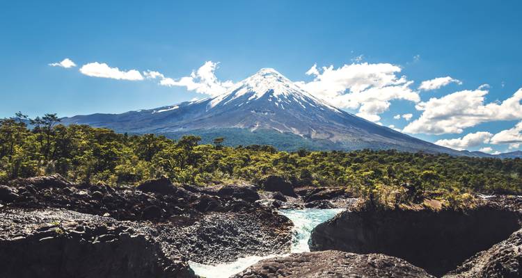 Volcan enneigé majestueux avec des rochers et une rivière au premier plan.