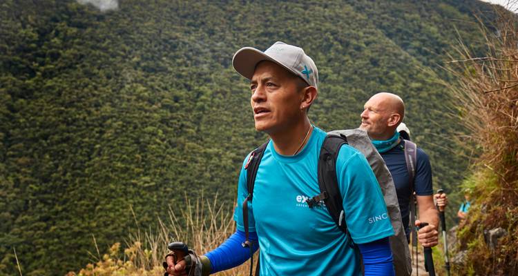 Guide conduisant des randonneurs à travers une forêt de nuages dense et verdoyante sur un sentier étroit.