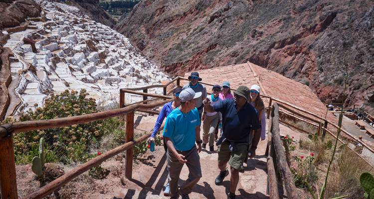 Petit groupe montant les marches en bois au-dessus des terrasses de sel de Maras, avec les parois rocheuses accidentées du canyon en arrière-plan.