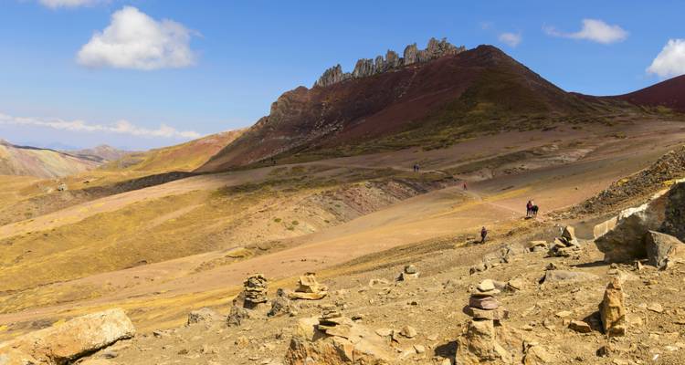 Les randonneurs traversent un paysage aride à haute altitude avec des crêtes dentelées rouges et jaunes sous un ciel bleu.