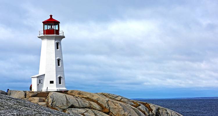 Witte vuurtoren met rode lantaarn op granietrotsen boven de oceaan in Peggy's Cove.