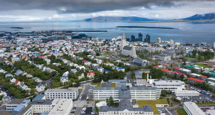 Aerial panorama of Reykjavik featuring Hallgrímskirkja church and colourful city blocks beside the bay.