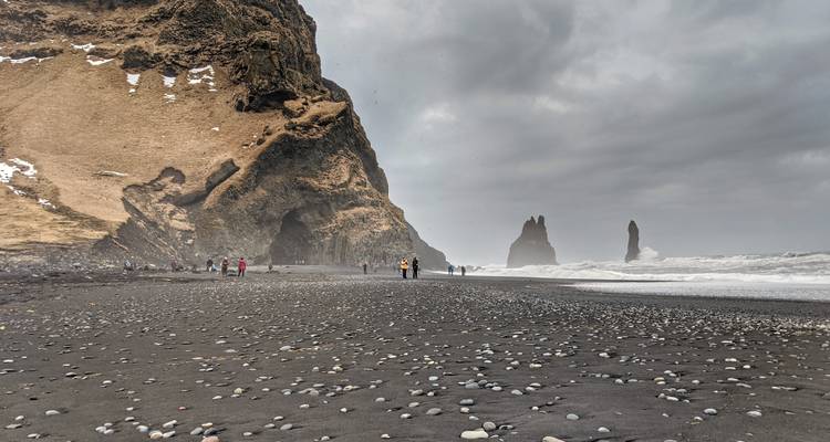 Stormy waves crash on the black sand of Reynisfjara beach with basalt sea stacks rising in grey mist.