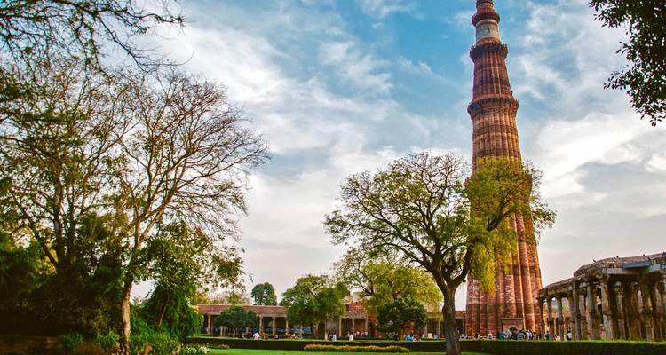 Qutub Minar umgeben von Gärten und Menschen, mit Bäumen und einem klaren Himmel.