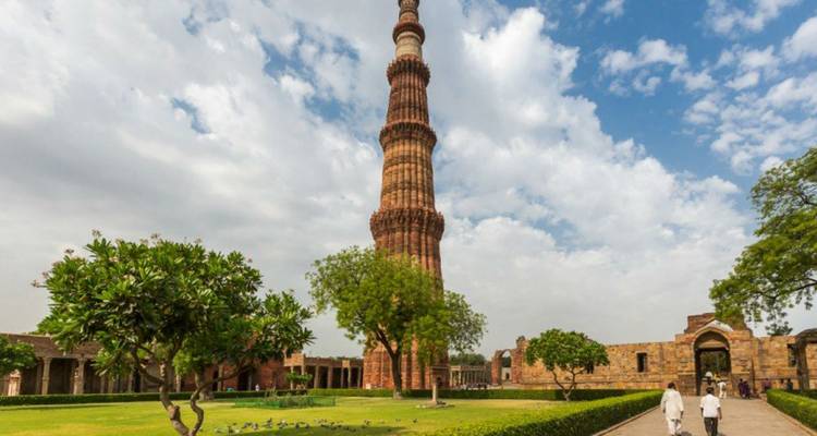 Qutub Minar erhebt sich über gepflegte Gärten mit Besuchern.