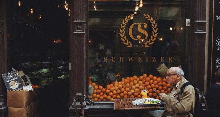 Homme mangeant à l'extérieur d'un café rempli d'oranges.