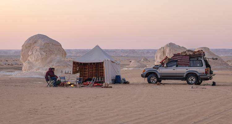 Installation de campement avec tente et véhicule dans un paysage désertique.