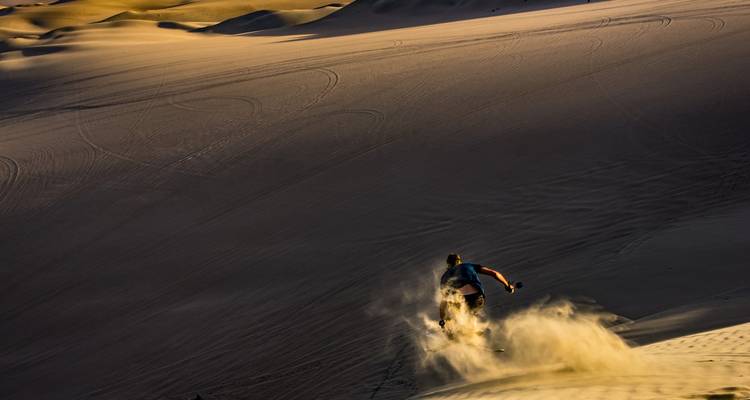 Descendre une grande dune en sandboard dans le désert.