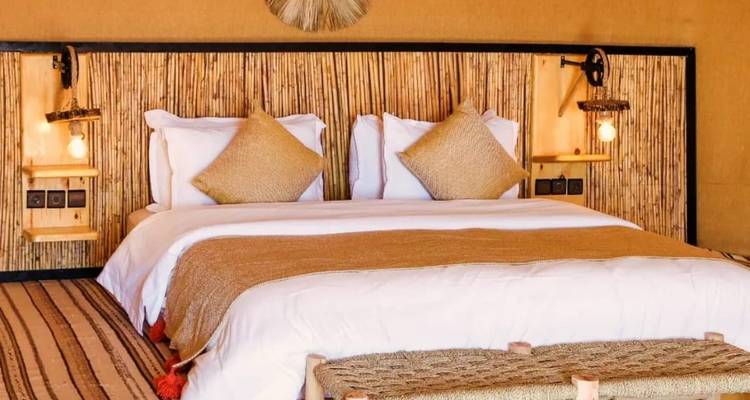 Chambre de camp du désert élégante avec tête de lit en bambou, textiles neutres et éclairage ambiant chaleureux.