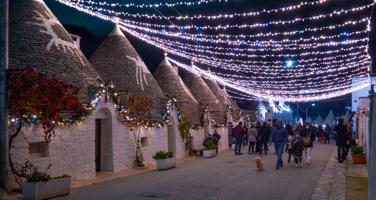 Une rue bordée de maisons trulli décorées de guirlandes lumineuses la nuit.