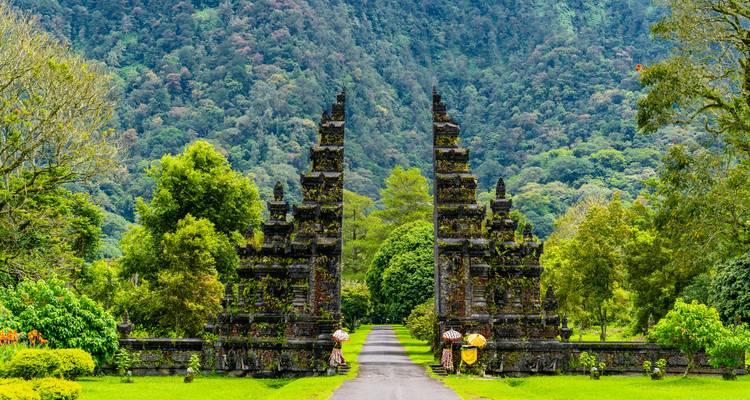 La puerta Handara simétrica que conduce a una avenida bordeada de árboles con una ladera de montaña verde de fondo en Bali.