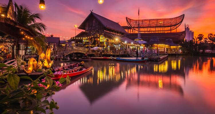 Mercado vibrante en la orilla del agua y edificios de madera que brillan al atardecer reflejados en el agua tranquila del canal.