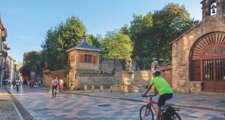 Un cycliste roule sur une place pavée entourée de bâtiments historiques.