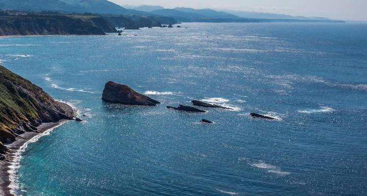 Vue côtière pittoresque avec falaises, océan et montagnes lointaines.