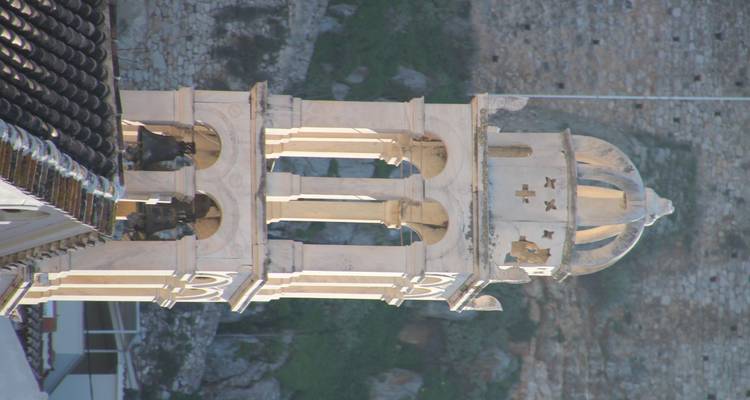 Torre de campanario con arcos y una cúpula contra un fondo de muro de piedra.