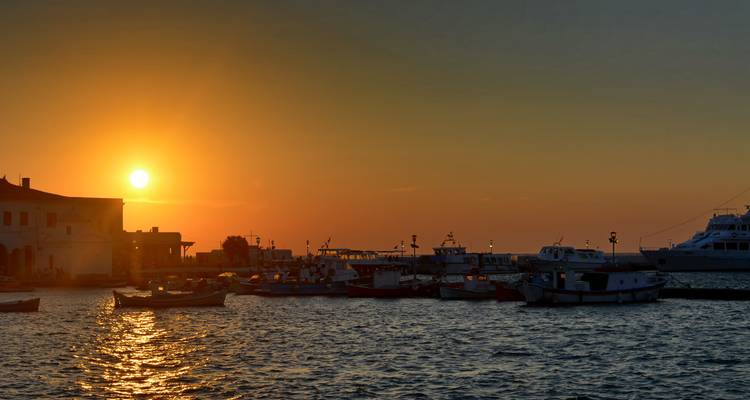 Coucher de soleil sur la mer avec des bateaux en silhouette.