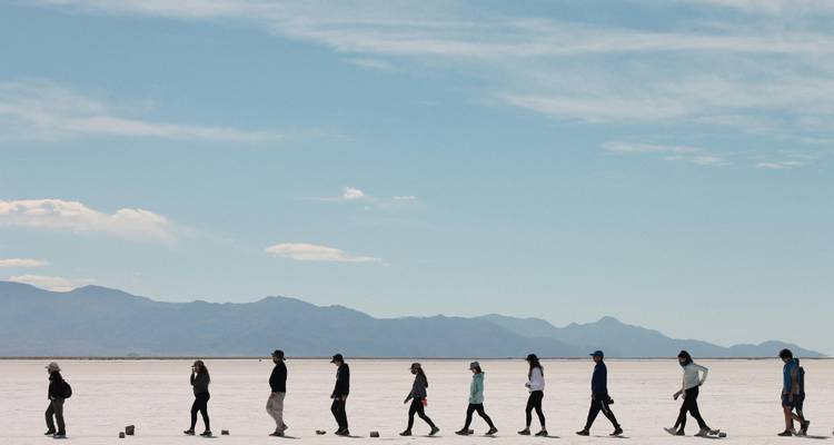 Personas caminando a través de un salar con montañas al fondo.