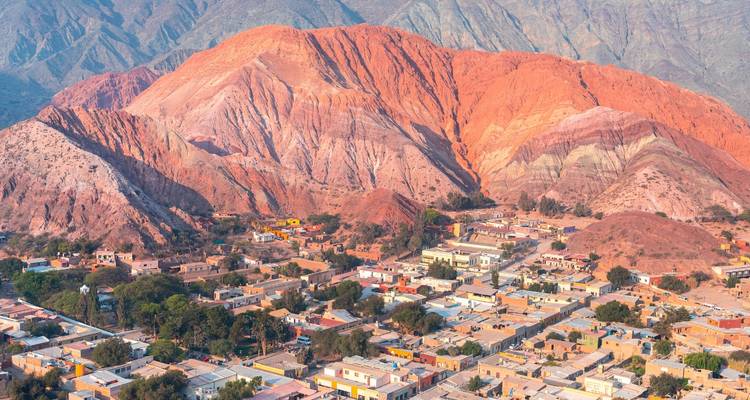 Colinas coloridas y pueblo al pie de una cadena montañosa.