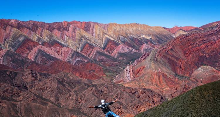 Persona posando con los brazos extendidos frente a montañas coloridas.