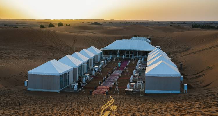 Campement dans le désert avec des tentes disposées en rangée au coucher du soleil.