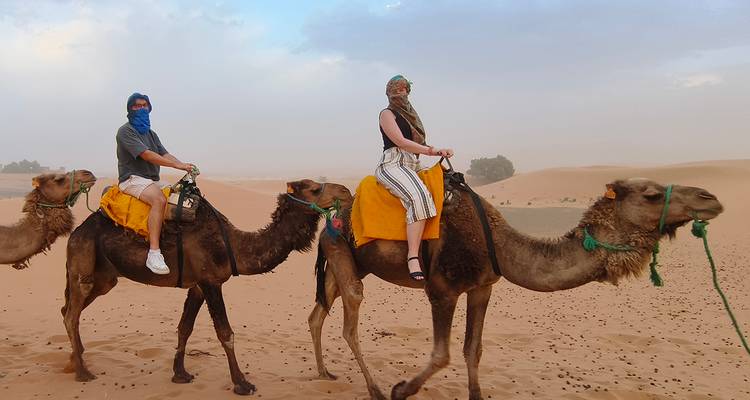 Dos personas montando camellos en un entorno desértico.