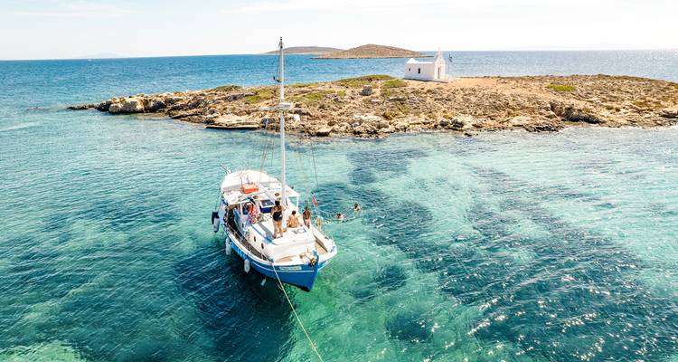 Petit bateau avec des personnes près d'une île avec une petite église, entouré d'eau claire.