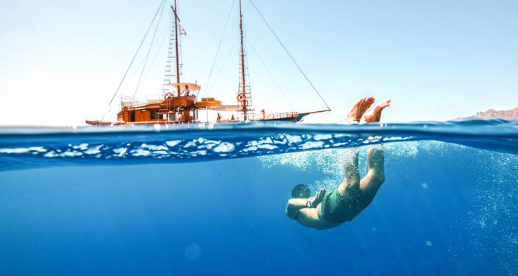 Personne plongeant dans l'océan avec un voilier en arrière-plan