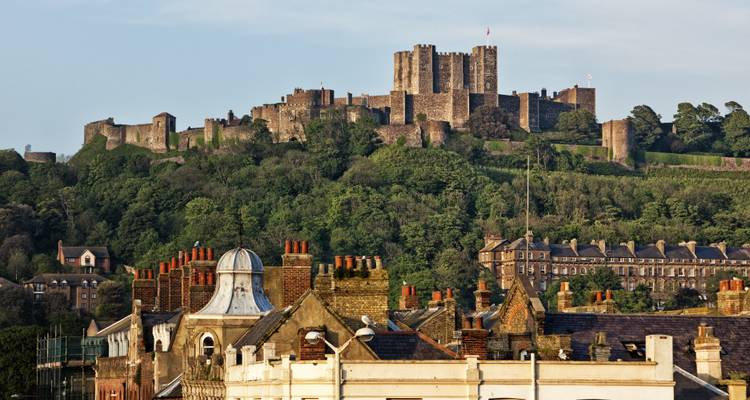 Un château fortifié sur une colline vu par-dessus des bâtiments à toiture.