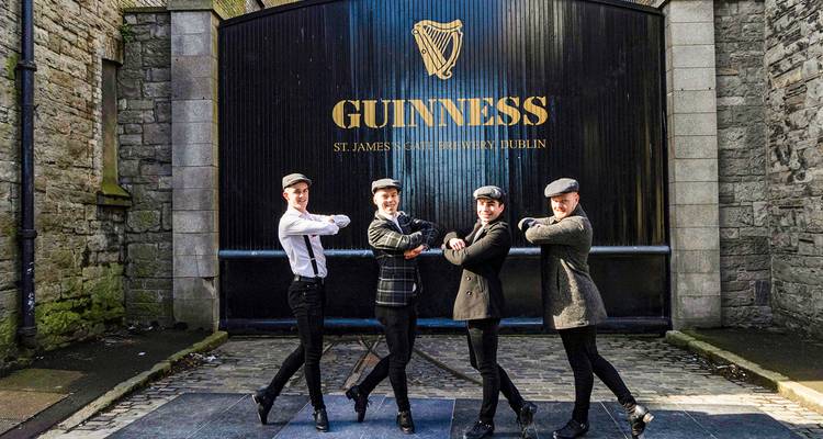 Quatre danseurs irlandais posent en plein mouvement devant l'entrée emblématique de la brasserie Guinness St James's Gate à Dublin.