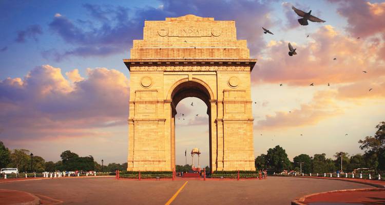 India Gate bei Sonnenuntergang mit Vögeln, die über den Himmel fliegen.
