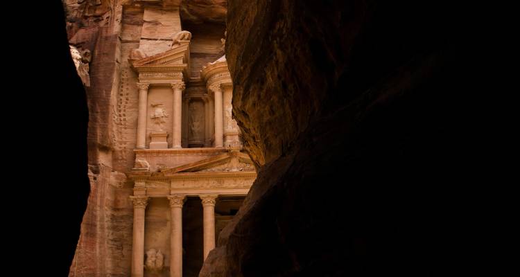 La icónica Tesorería de Petra vista a través de un estrecho siq bajo luz sombreada.