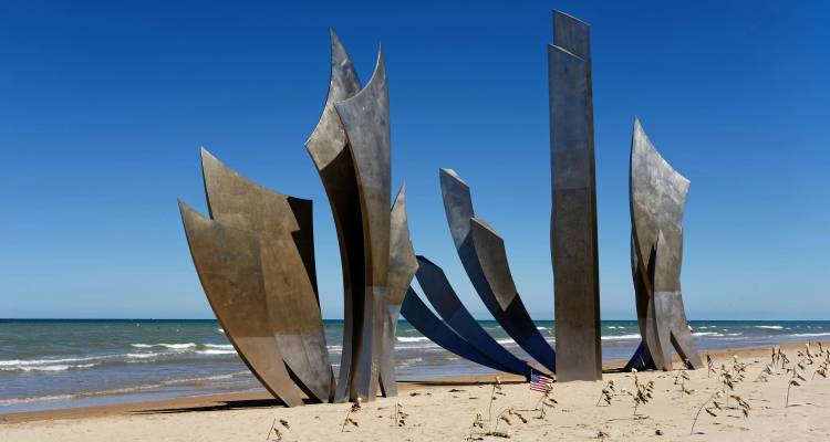 Sculpture métallique dramatique sur une plage avec un ciel bleu clair.