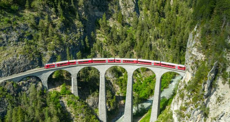 Tren rojo atravesando un pintoresco puente de piedra arqueado en las montañas.