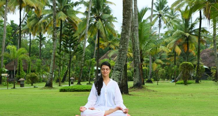 Mujer meditando en un entorno verde exuberante con palmeras.